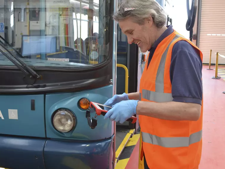 man using tablet next to a bus.