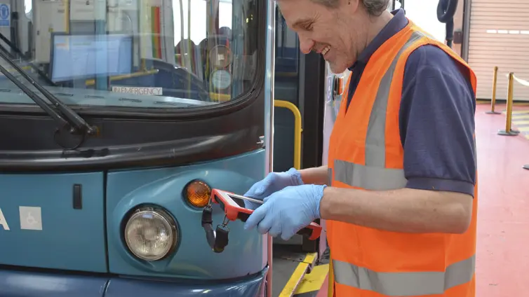 man using tablet next to a bus.
