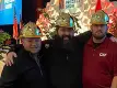 three men in gold hard hats smiling in front of a stage at the Precast Show