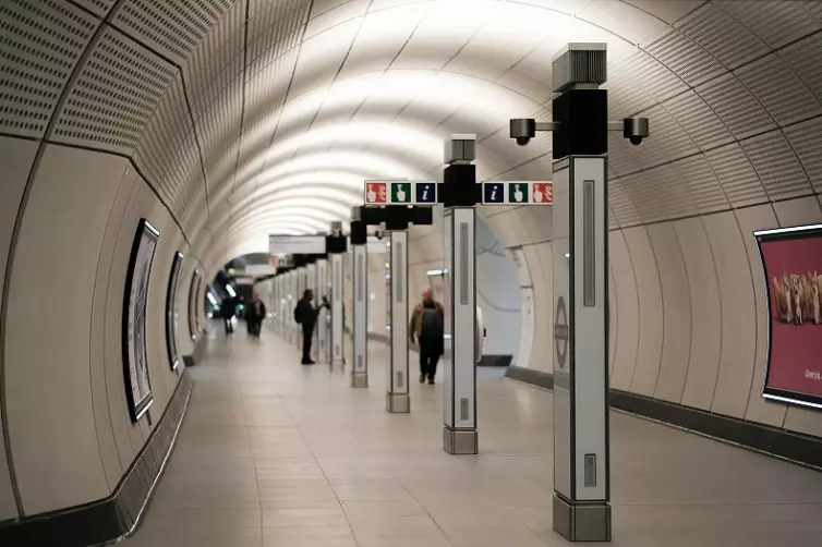 Elizabeth line underground station tunnel with signage to fire alarms and information.