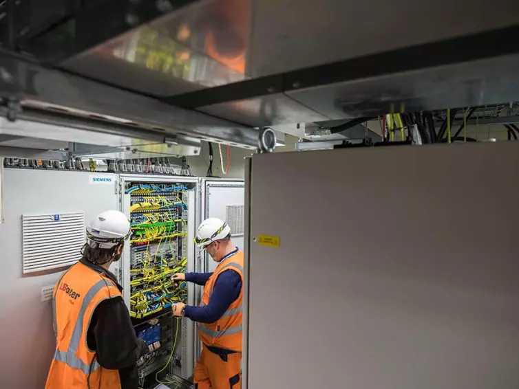 2 men installing telecoms equipment in station.