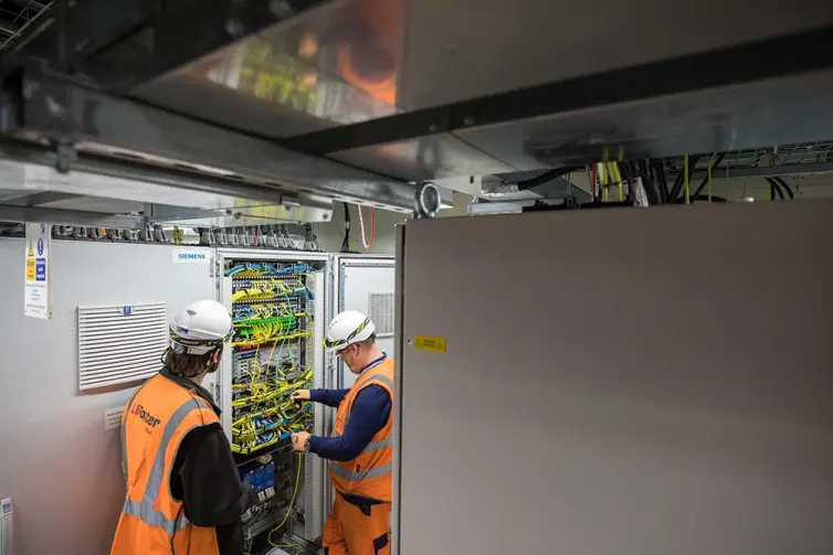 2 men installing telecoms equipment in station.