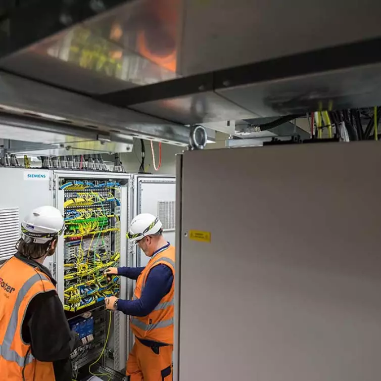 2 men installing telecoms equipment in station.