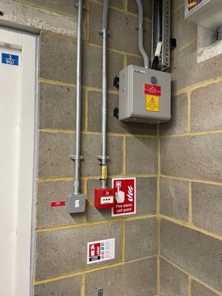 Fire alarm call point and light switch on a wall.