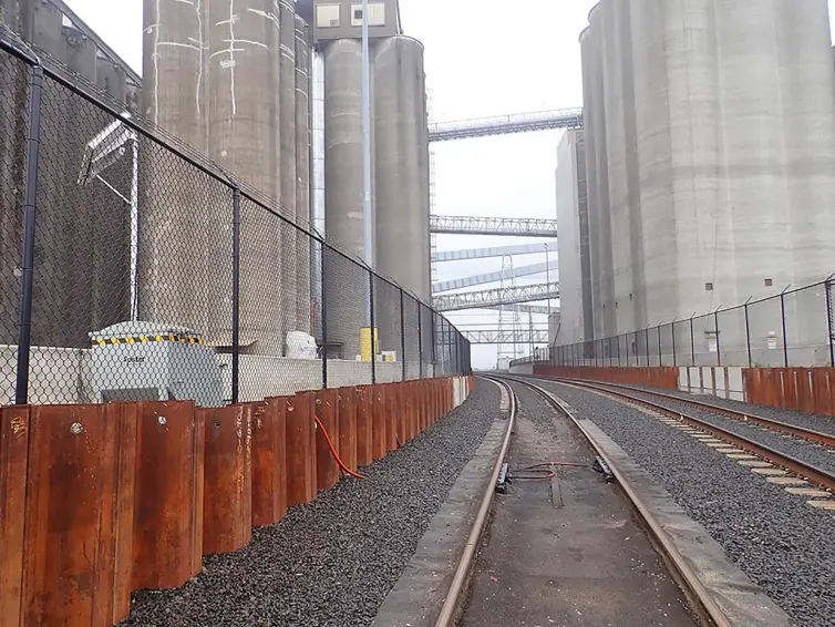 Industrial rail tracks running through grain elevator complex with monitoring equipment for freight car weight detection.