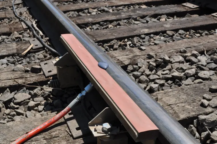 A close-up view of a railroad track where a puddle of purple-grey liquid is shown on an orange foam bar attached to the rail.