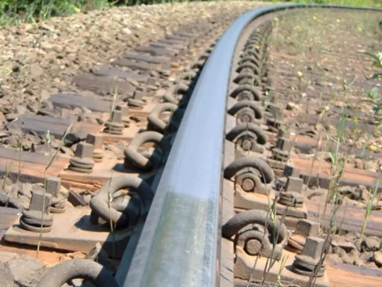 A close-up view of a curved railroad track where a layer of purple-grey material is covering the top of the rail.