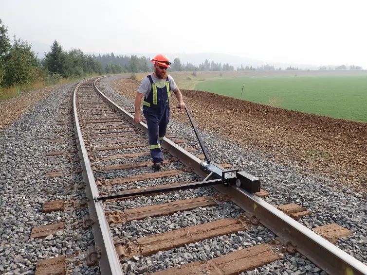 man walking on a railroad track with a device on the rail to test the performance.