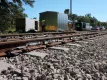 Railway workers in high-visibility safety gear installing WILD IV wheel impact detection equipment on railroad tracks, with strain gauges and red cables visible along the rails, and a white equipment trailer in the background.