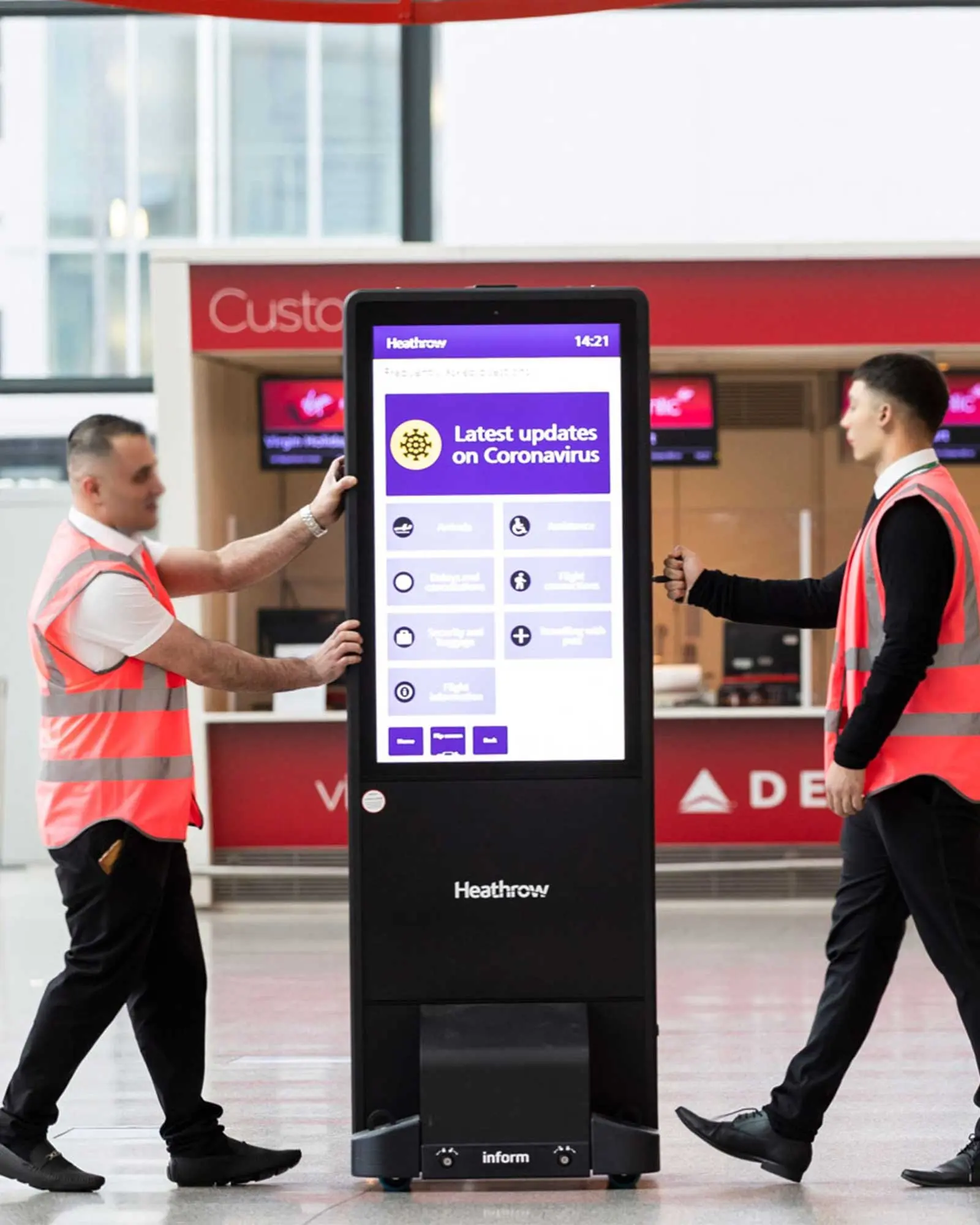 Two men moving a mobile inform totem in a railway station.