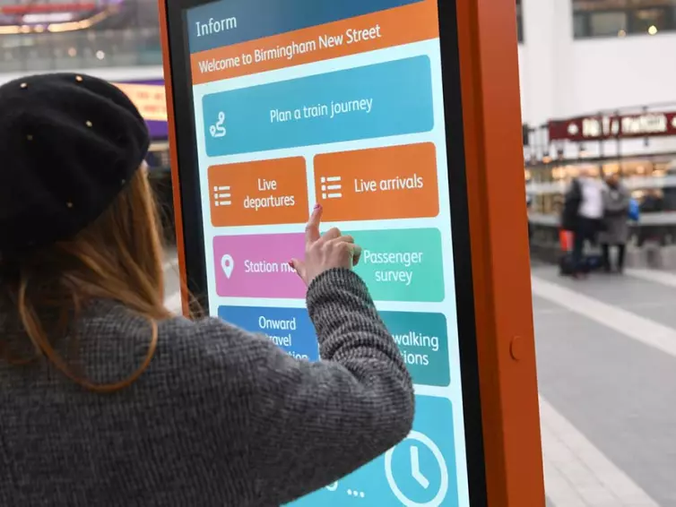 Lady using touchscreen totem in train station.