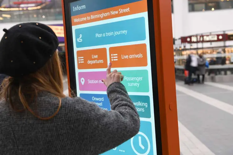 Lady using touchscreen totem in train station.
