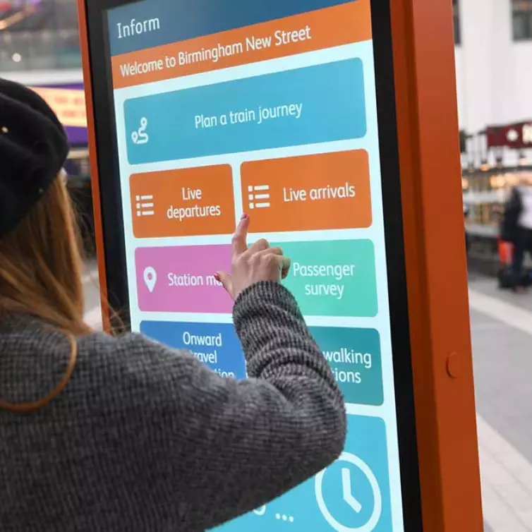 Lady using touchscreen totem in train station.