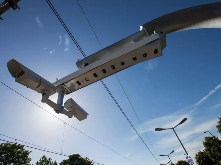 Traffic monitoring cameras mounted on a metal pole against a clear blue sky.