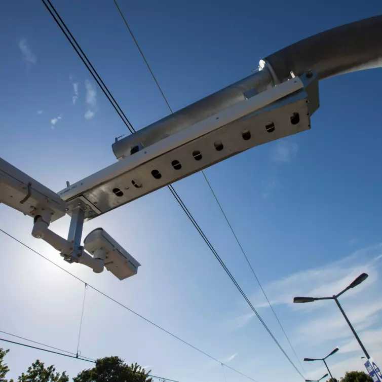 Traffic monitoring cameras mounted on a metal pole against a clear blue sky.