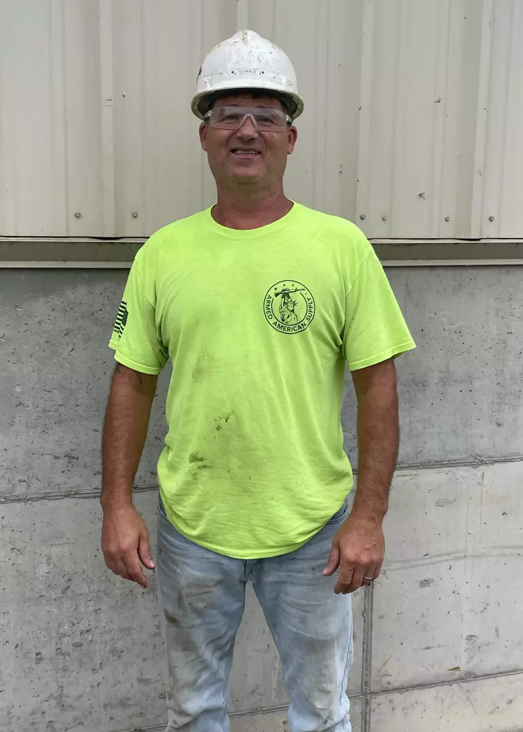 Man smiling wearing a high-vis bright green shirt, a white hard hat, and safety glasses.